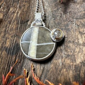 In Sterlingsilber gefasster Allgäuer Kieselstein mit schöner Zeichnung (schräges Kreuz) und einem in Gelbgold gefassten Diamant am Rand.