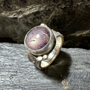 Handgeschmiedeter Ring mit einem runden Korund (Saphir/Rubin) mit kleinen goldenen Nieten und stark strukturierter Ringschiene